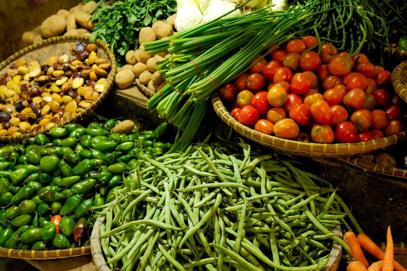 Crates piled high with fresh tomatoes, chillies, greens and carrots at market